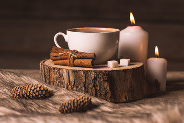 white cup with coffee, candles, cinnamon, sugar, fur and cones 