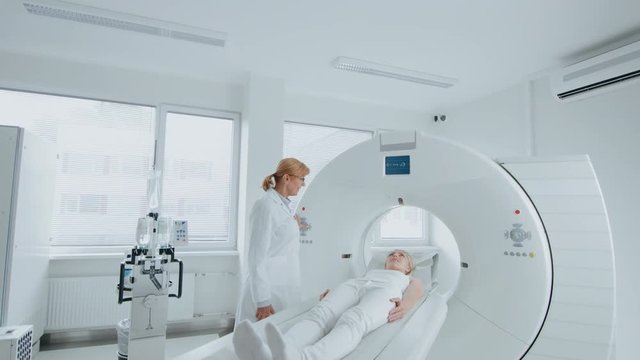 In Medical Laboratory Female Radiologist Controls MRI or CT Scan with Female Patient Undergoing Procedure. High-Tech Modern Medical Equipment. 