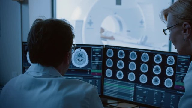 In Medical Laboratory Patient Undergoes MRI or CT Scan Procedure, in Control Room Doctor and Radiologist Discuss Diagnosis while Watching Procedure and Monitors Brain Activity