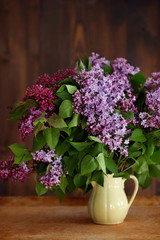 Home interior decor, bouquet of lilacs in a vase and books on rustic wooden table, on a white wall background.