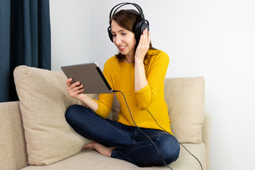 Beautiful women sitting in sofa and listening with headphones. E-learning concept.