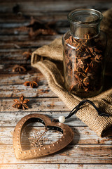 New bronze toy heart and glass jar with anise on a wooden old table. Rustic style.