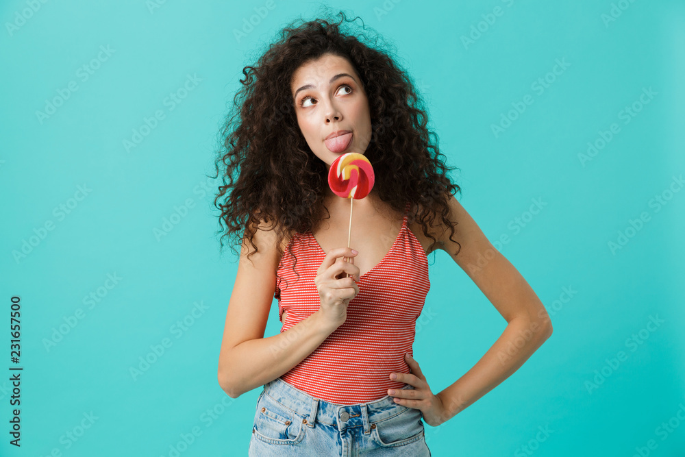 Poster Portrait of brunette woman 20s wearing casual clothing holding lollipop, isolated over blue background