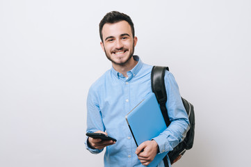Portrait of cheerful handsome man holding laptop and phone over white background and looking at the camera.