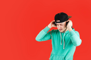 Pretty young emotional guy in headphones listening to music on isolated on red background