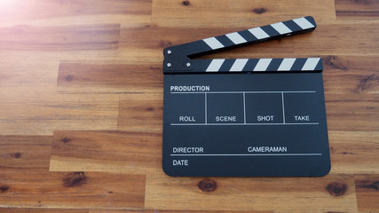 Clapper board or clap board or movie slate use in video production , film, cinema industry. It's black color on wood background with flare light.