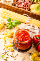 Glass jar with homemade classic spicy tomato pasta or pizza sauce with pine nuts and basil. Italian healthy food background.