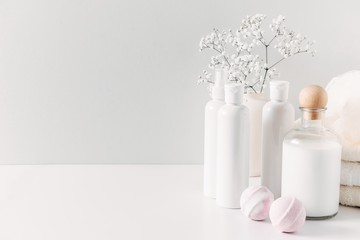 Soft light bathroom decor for advertising, design, cover, set of cosmetic bottles, bath accessories, white small flowers in vase, towel on white wooden shelf. mock up,copy space 