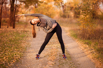 Young sportive woman doing exercises in autumn. Sportswoman stretching her body.
