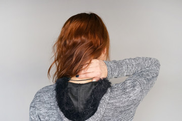 Close-up view of a young redhead woman with pain in the neck on gray background. Body And Health Care Concept.