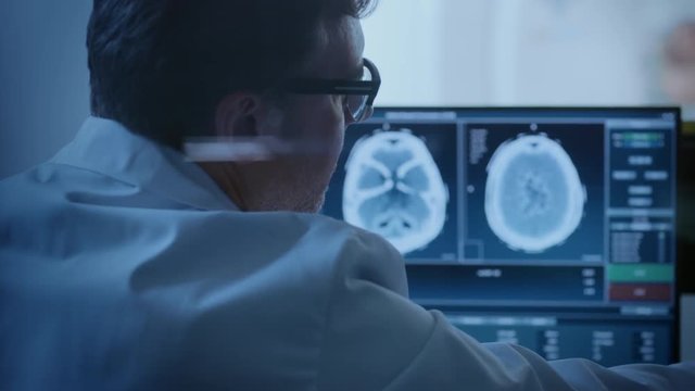 In Medical Laboratory Patient Undergoes MRI or CT Scan Process under Supervision of Radiologist in Control Room, He Watches Procedure and Monitors Brain Activity Results.