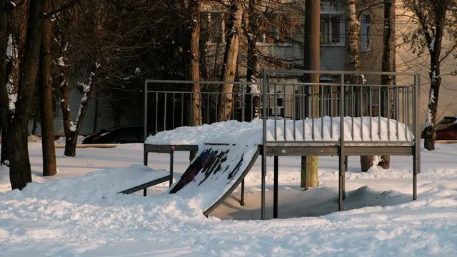 Skate boarding park in snowy sunny winter city Park. Snow drifts on the hill to skateboard.
