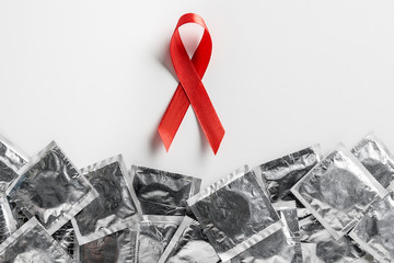 top view of aids awareness red ribbon and silver condoms on white background, medical concept