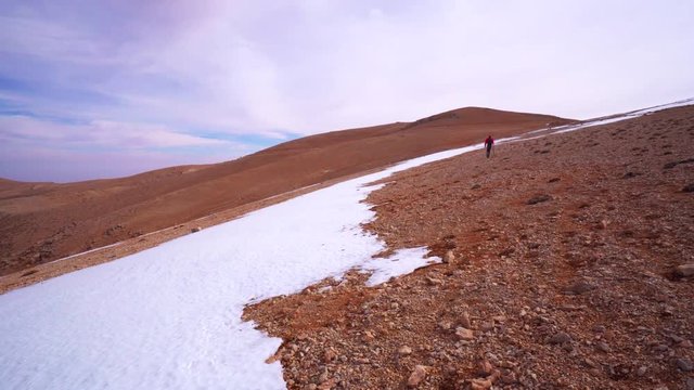 Man hiking in arid beautiful landscape next to small photogenic patch of fresh snow