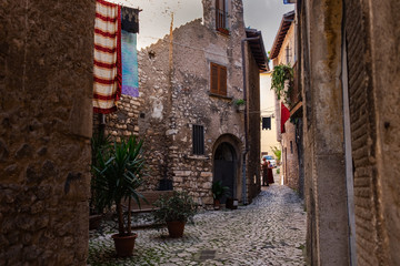 A narrow  traditional street paved with stone among stone houses in a medieval small town Sermoneta not far from Rome. The laundry is drying in the street and flags are hanging