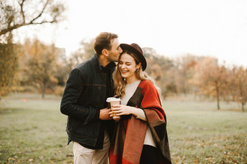 Young couple in love hugging, having fun and smiling in the park on a sunny autumn day and drinking tea