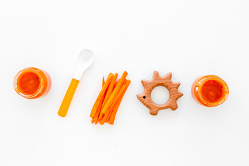 Healthy food for small babies. Carrot puree in bowl near carrot slices, spoon, toy on white background top view copy space