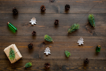 New Year pattern with pine sprigs, cones, spruce figure, fir oil and new year gift decorated with craft paper and pine sprout on dark wooden background top view