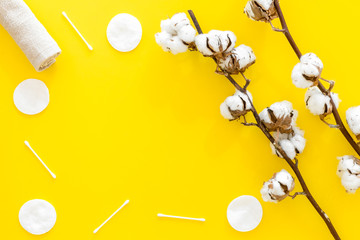 Fototapeta premium Products made of cotton. Bath accessories. Towels, cotton pads and swabs near dry cotton flowers on yellow background top view copy space frame