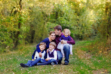 Fototapeta premium Portrait of young parents with three children. Mother, father, two kids brothers boys and little cute toddler sister girl having fun together in autumn forest. Happy family of five