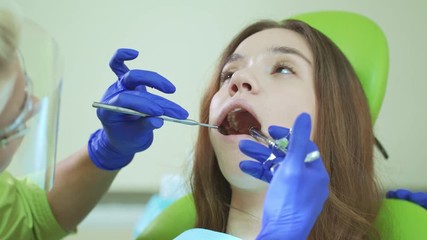 Young woman with open mouth during dental procedure. Anesthetic injection in patient tooth. Dentist using mouth mirror and medicine syringe. Dental anesthesia and treatment