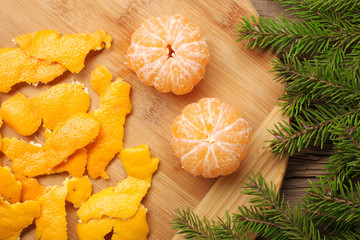 Fresh peeled and unpeeled mandarins or tangerines on the wooden table with Xmas tree branches