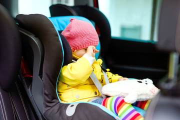 Adorable tired crying baby girl in colorful clothes sitting in car seat. Toddler child in winter clothes going on family vacations and jorney. car in traffic jam