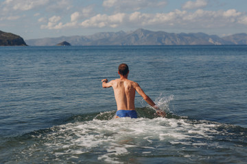 A young man going swim in the sea against the backdrop of mountains
