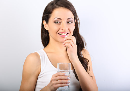 Happy smiling positive woman eating the pill and holding the glass of water in the hand on white background. Closeup portrait