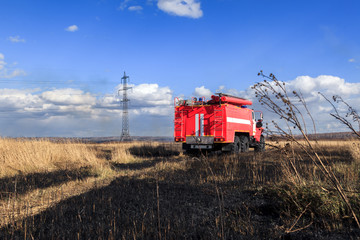 Obraz premium Red firetruck car Ural rides through the autumn field with yellow and faded grass against the blue sky and clouds. The concept of extinguishing forest fires in USA