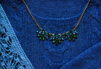 Knitting and hand made concept-blue knitted sweater and green necklace with gold chain close-up. Knitting texture. Part of knitted clothing. Autumn, winter concept. Top view, copy space, flat lay.