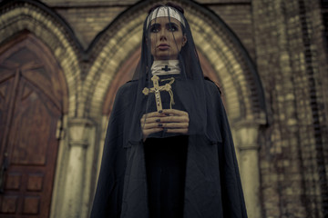 Naklejka premium Young nun is standing and praying with cross in her hands on temple background.