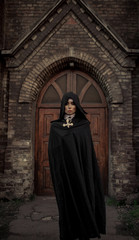 Beautiful young nun is standing and praying with cross in her hands on temple background.