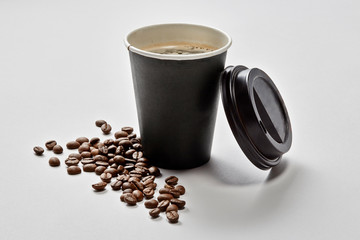 Vaso de café para llevar con tapa apoyada y granos de café alrededor
