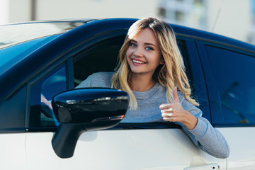 portrait of blond smiling woman showing thumb up while driving car