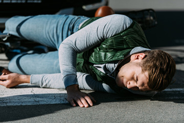 injured young cyclist lying with bicycle on road after car accident