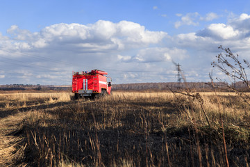Fototapeta premium Red firetruck car Ural rides through the autumn field with yellow and faded grass against the blue sky and clouds. The concept of extinguishing forest fires in USA