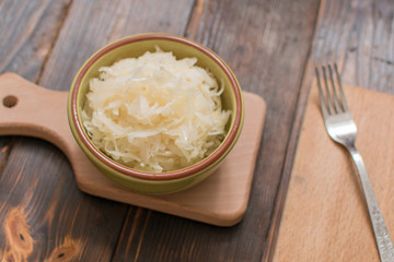 Sauerkraut in a plate on a wooden background.
