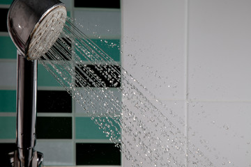 Shower head splashing water with water drops flowing in bathroom.