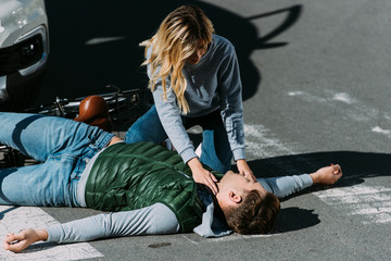 young woman checking pulse of injured cyclist after traffic collision