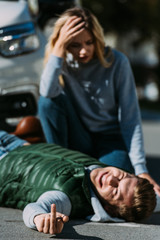 Fototapeta premium injured young man lying on road and showing middle finger after traffic collision