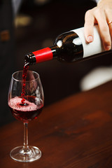 Waiter pouring red wine into wineglass. Sommelier pours alcoholic drink