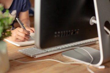 Hands of a Business woman is writing book as notepad or Take notes on Her wooden table desk  . Business Success Working at home office with notebook and computer for marketing and part time Concept.
