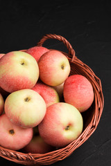 Ripe raw apples in wicker basket on black background with copy space - organic yellow and red fruits.