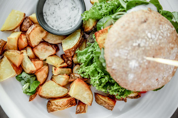 Vegan burger with lettuce, tomatoe, fried potatoes and garlic dill sauce