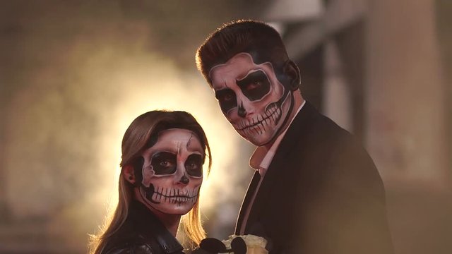 Couple with dark skull makeup on the background of burning fire and smoke. Halloween face art. Halloween concept. Zombie. Silhouette. Slow motion.
