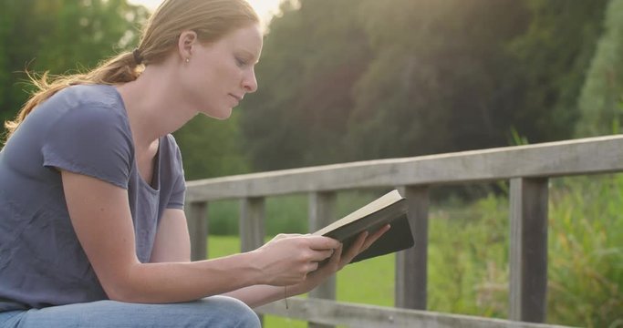 A young Christian woman reading the Bible and praying in a park.