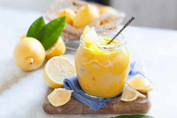 Homemade fresh lemon curd in jar with sliced lemon fruits on wooden board, selective focus