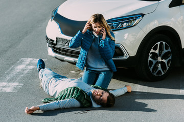 high angle view of scared young woman looking at injured man and calling emergency after car...