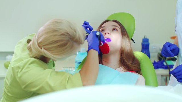 Stomatologist using lamp for polymerization of dental materials. Dentist using dental curing UV light in clinic. Woman patient with open mouth in dentist chair. Modern dental medicine